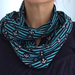 Könnte beinhalten: Ein Loop-Schal mit einem Muster aus dunkelblauen und leuchtend türkisfarbenen Streifen. Der Stoff ist mit kreisförmigen Aufnähern verziert, die weiße Ankersymbole enthalten und gleichmäßig über den gestreiften Hintergrund des Schals verteilt sind.