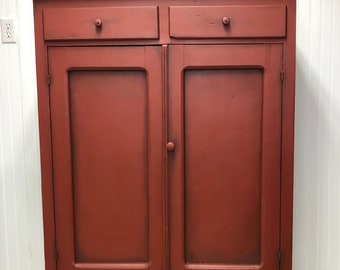 May include: A red painted antique cabinet with two drawers and two doors. The cabinet has a distressed finish and is made of wood.