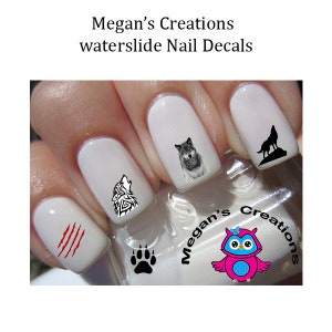 Peut inclure: Des autocollants pour ongles en décalcomanie à l'eau représentant un loup hurlant, une silhouette de loup, une empreinte de patte de loup et des marques de griffes rouges. Les autocollants sont présentés sur un ensemble d'ongles peints.
