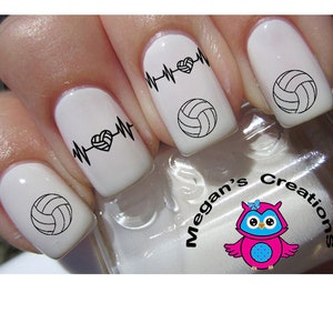 May include: White nail polish with black volleyball and heartbeat designs. The nails feature a volleyball and a heartbeat design with a volleyball in the center. The image also includes the text "Megan's Creations" and a cartoon owl.