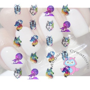 May include: Nail art decals featuring watercolor wolf designs in various poses and colors. The decals include images of wolf faces, wolves howling at the moon, and colorful accents. The nail art is applied to white nail polish.