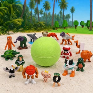 May include: A large, spherical, light green bath bomb surrounded by a collection of small, colorful plastic animal and creature figurines, including a shark, elephant, monkey, and various hybrid characters, arranged on a sandy surface.
