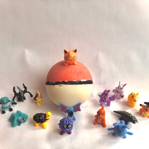 May include: A collection of colorful cartoon character figurines, including a red, white, and orange bath bomb with a small orange figurine on top. The figurines are arranged on a white surface.