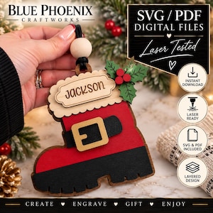 May include: A wooden Christmas stocking ornament featuring a red boot with a black sole and belt, a gold buckle, and a white scalloped cuff engraved with the name Jackson. It includes green holly leaves with red berries and a wooden bead hanger.
