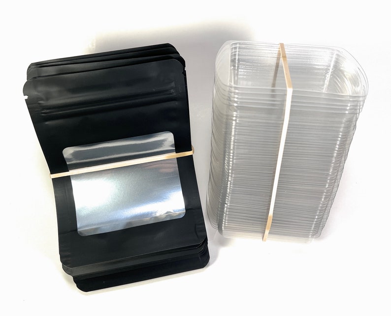 Peut inclure: Une pile de sachets en plastique noir debout avec une fen&ecirc;tre transparente et une pile de contenants en plastique transparent.