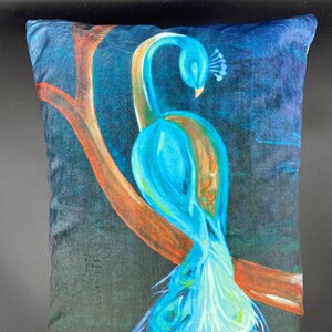 May include: A blue and green peacock pillow with a dark background. The peacock is perched on a branch with its tail feathers spread out.
