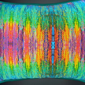 Op de afbeelding: Een kleurrijk kussen met een turquoise rand en een levendig abstract ontwerp met strepen in geel, oranje, rood, paars en blauw. Het ontwerp is symmetrisch en heeft een glinsterende textuur.