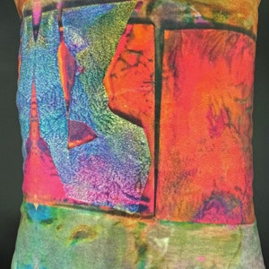 May include: Rectangular decorative pillow with an abstract design. The pillow features a vibrant mix of colors, including red, orange, blue, green, and pink. The design appears to be a blend of geometric shapes and organic forms, creating a unique and artistic look.