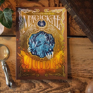 Peut inclure: Une couverture de livre illustrée en or et brun avec le texte "Wishing you a Magical Yule" et une illustration d'un oiseau bleu et blanc.