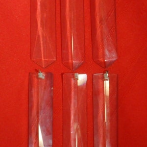 Puede incluir: Seis prismas de cristal de vidrio transparente con un lazo de metal plateado en la parte superior. Los prismas son de forma rectangular con un extremo puntiagudo.