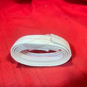 May include: A coiled length of white woven fabric tape featuring a thin, continuous red stitched line running horizontally along the center of the material. The tape is secured with a small piece of clear adhesive tape on the outer edge.