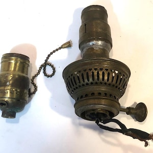 May include: Two antique brass lamp parts. One is a socket with a pull chain, the other is a larger lamp base with a decorative pierced design. The parts show signs of age and wear.
