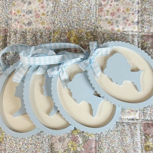 May include: Four light blue oval-shaped wooden frames with scalloped edges. Each frame features a white silhouette of a person's head and shoulders.