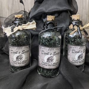May include: Three small glass bottles with cork stoppers and black wax seals. Each bottle contains green dried herbs and has a label that reads "CC18 Devil's Snare" with a small illustration of a frog. The label also reads "Constricts or strangles anything that touches it."