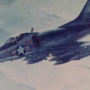 May include: A blue and gray military jet plane with a white star and red stripes on the side. The plane is flying in the sky with clouds in the background. The plane has the word "NAVY" on the side.