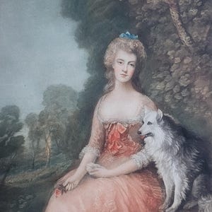 May include: A woman in a pink dress sits in a forest setting with a white dog. She is wearing a blue ribbon in her hair and holds a small red flower in her hand.