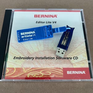 May include: A clear CD case containing embroidery software. The case holds a CD with the text "Embroidery Installation Software CD" and a blue USB drive and a blue dongle. The brand name "BERNINA" is visible.