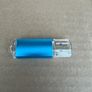 May include: A blue USB flash drive with a clear plastic connector. The body of the drive is a solid, bright blue color. The connector end has a standard USB port design.
