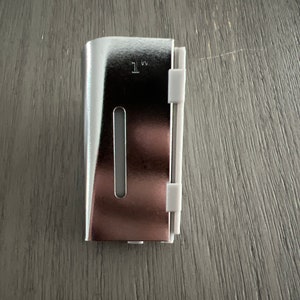 May include: A silver metal clip with a rose gold interior and a white plastic component. The clip is approximately 1 inch in length. The clip has a rectangular shape with a long, narrow opening.