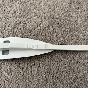 May include: White plastic door stop with a sliding latch. The door stop is shaped like a wedge and has a handle on the top.