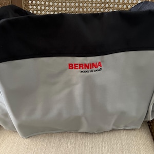 May include: A gray and black Bernina sewing machine carrying case with the text "Bernina made to create" embroidered on the front.