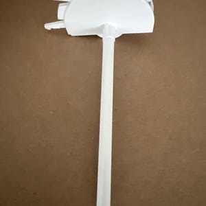 May include: A white plastic kitchen utensil with a long, cylindrical handle and a semi-circular head. The head has a flat surface and two small, protruding arms. The utensil is designed for food preparation.
