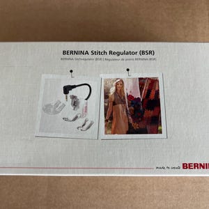 Op de afbeelding: Een rechthoekige doos met de tekst "BERNINA Stitch Regulator (BSR)". De doos heeft twee afbeeldingen, een van naaimachineonderdelen en een andere van een vrouw. De rechter benedenhoek van de doos heeft het woord "BERNINA" in het rood.