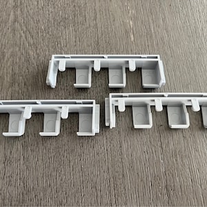 May include: Three white plastic pieces with multiple holes, each piece has five holes, the pieces are designed to be connected together.