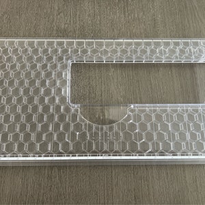 May include: A clear plastic sewing machine extension table with a honeycomb pattern and a ruler along the bottom edge. The ruler is marked in inches.
