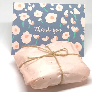 May include: A pink gift box tied with brown twine and a small card with a floral pattern and the text "Thank you".