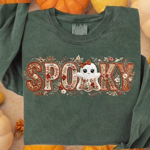 Pode incluir: Uma camisola de manga comprida verde escuro com a palavra "SPOOKY" bordada na frente. As letras são preenchidas com desenhos florais e um simpático personagem fantasma. O design apresenta cores laranja, branco e castanho, perfeito para o Halloween.