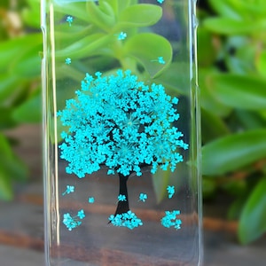 May include: A clear phone case with a blue flower design. The flowers are arranged in the shape of a tree.