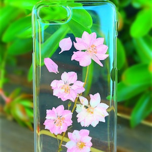 May include: A clear phone case with pink pressed flowers inside. The flowers are arranged in a cluster and have a delicate, natural look.