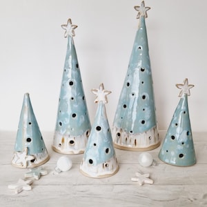 Könnte beinhalten: Satz von fünf Keramik-Weihnachtsbaumschmuck in verschiedenen Größen. Die Bäume sind hellblau mit weißen Flecken und haben Löcher. Die Spitzen der Bäume sind mit weißen Sternen verziert.