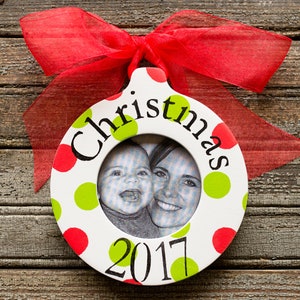 May include: White round Christmas ornament with red and green polka dots. The ornament has a photo frame with a picture of a mother and child. The ornament also has the text "Christmas" and "2017" written on it.
