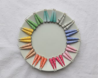 May include: A collection of 12 pairs of handmade paper earrings in a rainbow of colors. The earrings are displayed on a white plate. The earrings are made of rolled paper and have a variety of patterns.