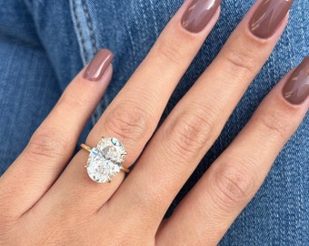 May include: A gold ring with a large oval-shaped clear gemstone. The ring is on a person's finger, which is wearing brown nail polish.