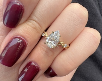 May include: A pear-shaped diamond engagement ring with a delicate, twisted band. The ring is set in gold and features small accent diamonds on the band.