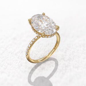Puede incluir: Un anillo de compromiso de oro con un gran diamante central de forma ovalada y un halo de diamantes más pequeños. La banda también está engastada con diamantes más pequeños.