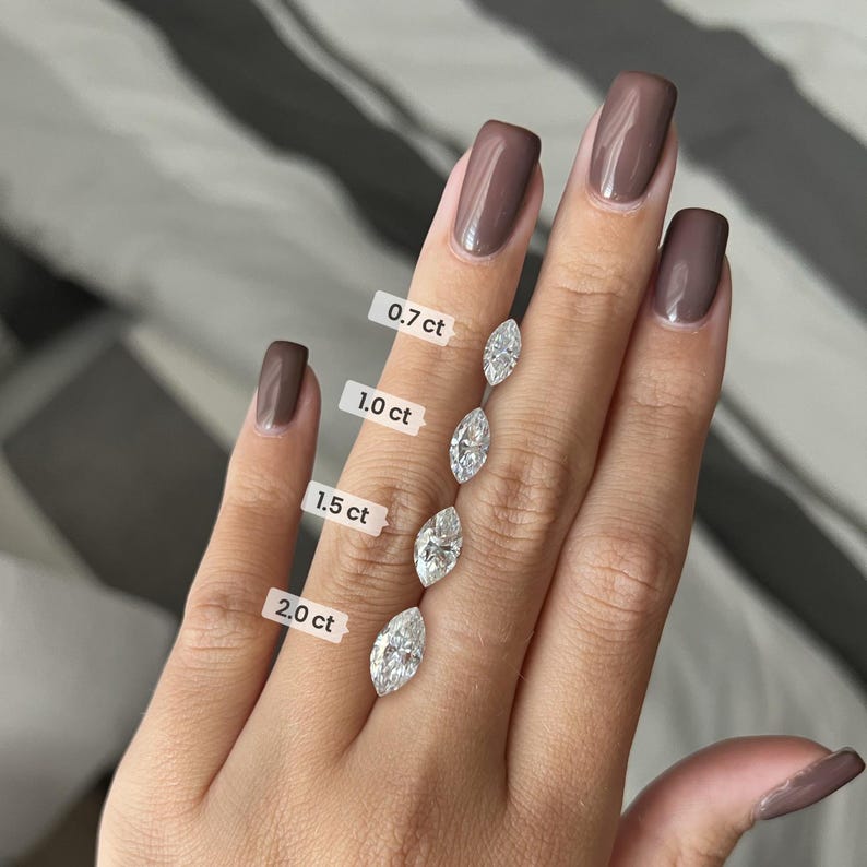 May include: A hand model wearing brown nail polish displays four marquise-shaped diamonds of different sizes. The diamonds are labelled with their carat weight: 0.7ct, 1.0ct, 1.5ct, and 2.0ct.
