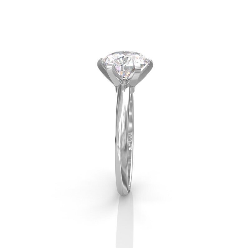 Pu&ograve; includere: Un anello di fidanzamento in argento con un grande diamante rotondo e chiaro incastonato in una montatura a quattro griffe. La fascia &egrave; una fascia semplice e dritta.