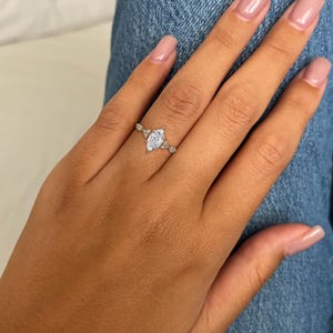 May include: A silver ring featuring a marquise-shaped clear stone and smaller clear stones on the band.
