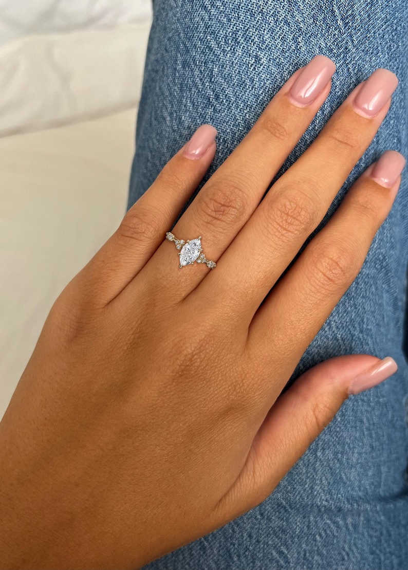 May include: A silver ring featuring a marquise-shaped clear stone and smaller clear stones on the band.