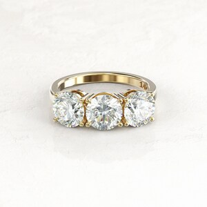 Close low-angle front view of a two-tone three-stone moissanite engagement ring, showing yellow gold prongs and inner settings, a white/silver-colored band, and a 14K stamp.