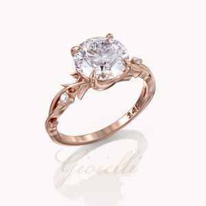 May include: A rose gold engagement ring with a large round center stone and two smaller accent stones. The band is intricately designed with a vine-like pattern.