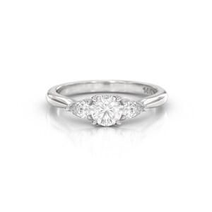 May include: A silver ring with a large, round, clear gemstone in the center, flanked by two smaller, pear-shaped gemstones. The ring band is smooth and polished.