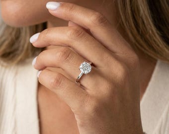 May include: A silver-toned ring featuring a single, large, round-cut clear gemstone set in a four-prong setting on a slender, polished metal band. The ring is worn on a finger, showcasing the brilliant, faceted surface of the central stone.