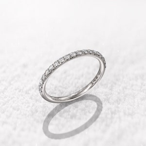 May include: A thin silver band with a row of small diamonds set around the entire ring.