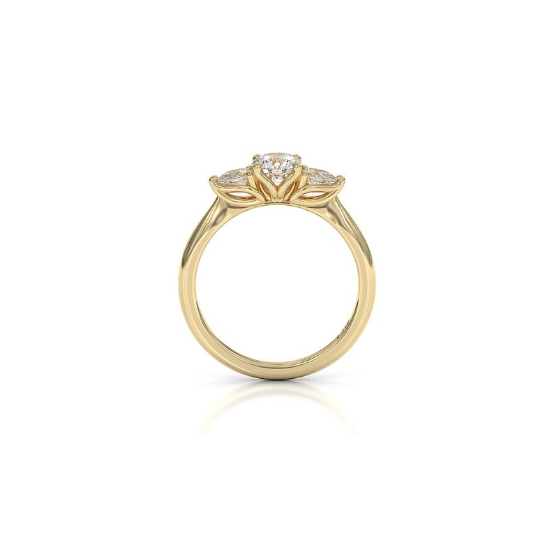 May include: A gold ring with a three-stone design. The center stone is round, flanked by two smaller, pear-shaped stones. The band is smooth and polished, creating a classic and elegant look. This ring is a piece of fine jewelry.