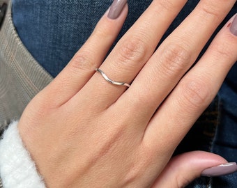 May include: A silver, wavy, thin ring on a finger with nude nail polish.